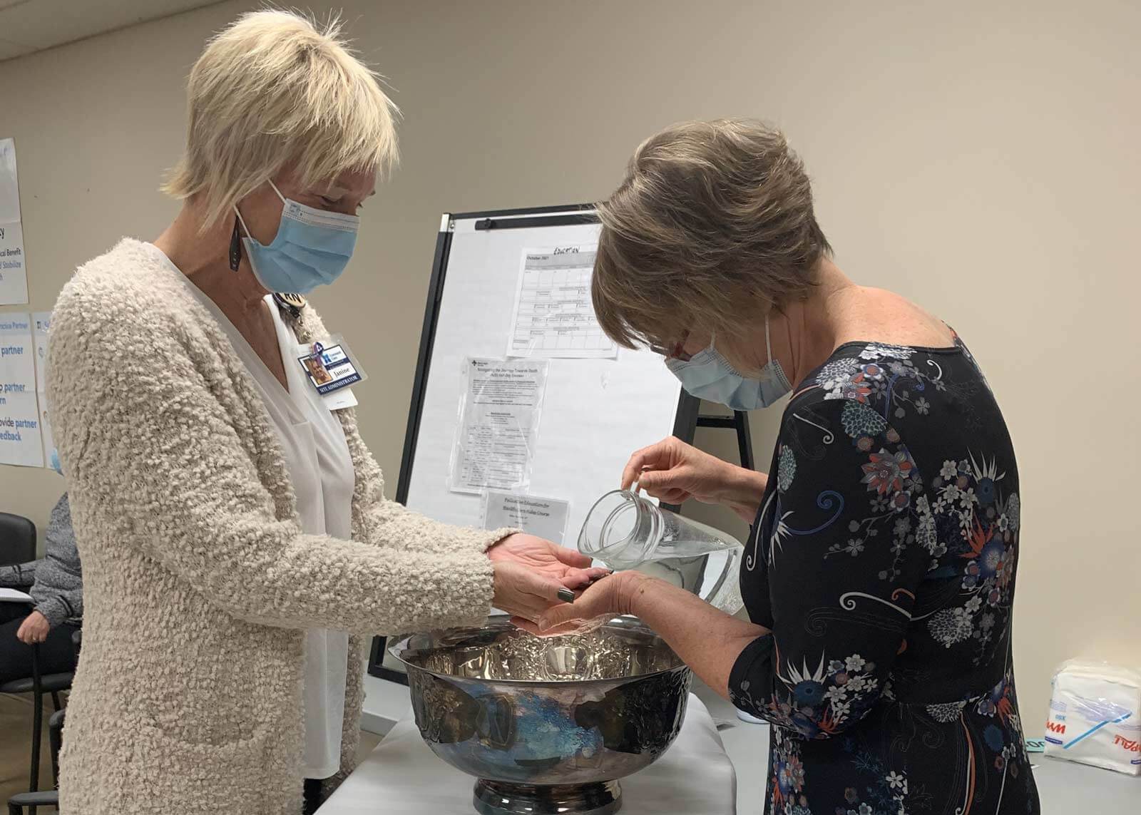 A chaplain about to pour water from a pitcher on the hands of a Covenant Health colleague over a metal basin