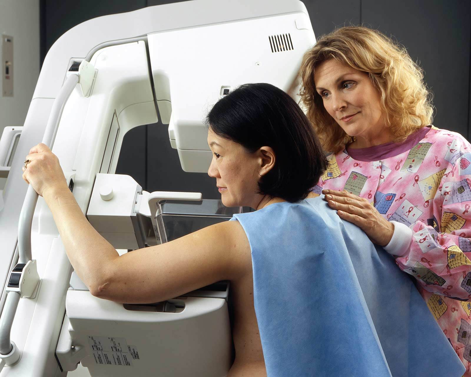 A healthcare worker places a reassuring hand on the shoulder of a woman during a mammogram