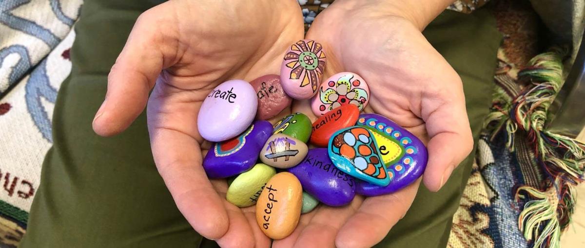 Hands cradling rocks painted with images and words such as create, healing, kindness, and accept