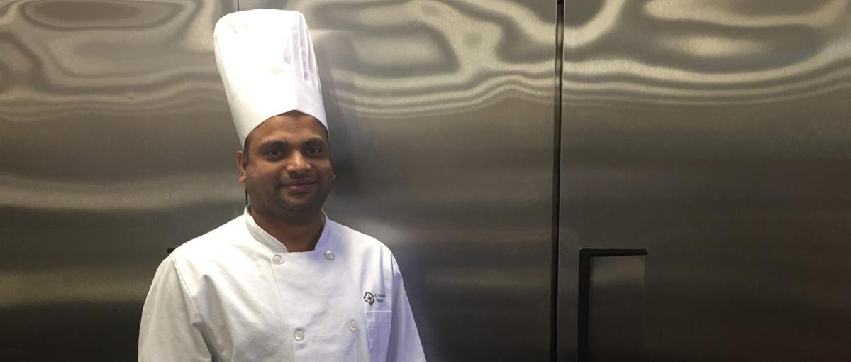 Joseph Vellam in a Covenant Health chef uniform posing in front of stainless steel fridges