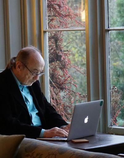A senior works on a laptop at a dining table.